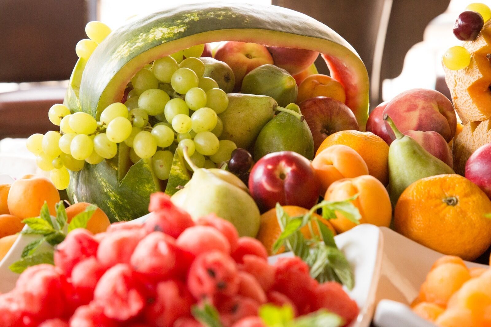 A variety of fresh fruits and vegetables, including grapes, apples, peaches, and oranges, displayed in a market setting.
