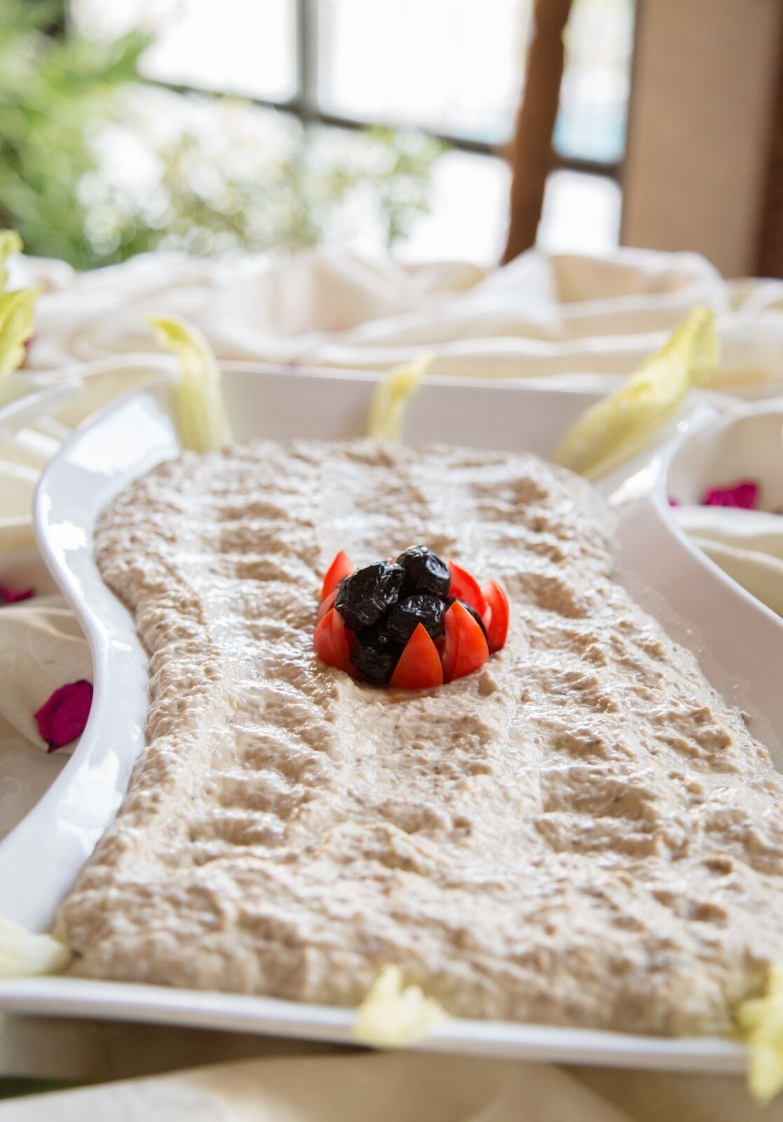 Ein Dessertteller mit cremigem Aufstrich und einer dekorativen Anordnung aus schwarzen Oliven und roten Tomaten.