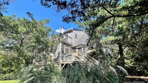 A two-story house with a wooden deck and a satellite dish. - Neaptide: Secluded & Spacious Home in Jackson Dunes (Ocracoke)