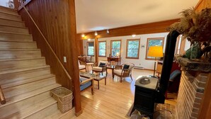 A spacious living area with a wooden staircase, a fireplace, and a dining area with chairs and a table. - Neaptide: Secluded & Spacious Home in Jackson Dunes (Ocracoke)
