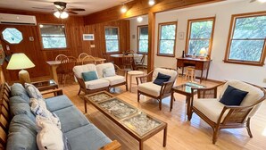 A cozy living room with a sofa, chairs, a coffee table, and a dining area with a table and chairs. - Neaptide: Secluded & Spacious Home in Jackson Dunes (Ocracoke)