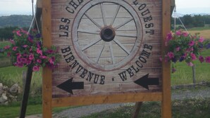 A wooden sign with a wheel design, featuring the text "LES CHAMBERES DE LOUISVILLE" and "WELCOME" with directional arrows. - LES CHAMBRES DE L'OUEST (Longessaigne)