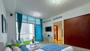 A modern hotel room with a large bed, a desk, a TV, and a view of a cityscape. - Big Studio w/ Balcony and easy access to the Beach in Marina (Dubai)