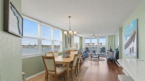 A spacious dining area with a wooden table and chairs, a chandelier, and large windows offering a view of the cityscape.