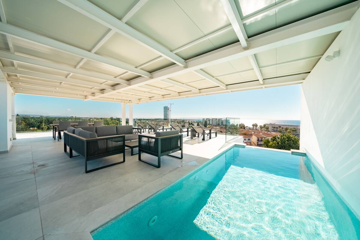 Piscina infinita en la azotea con vistas al horizonte de la ciudad, zona de estar al aire libre y un patio cubierto.