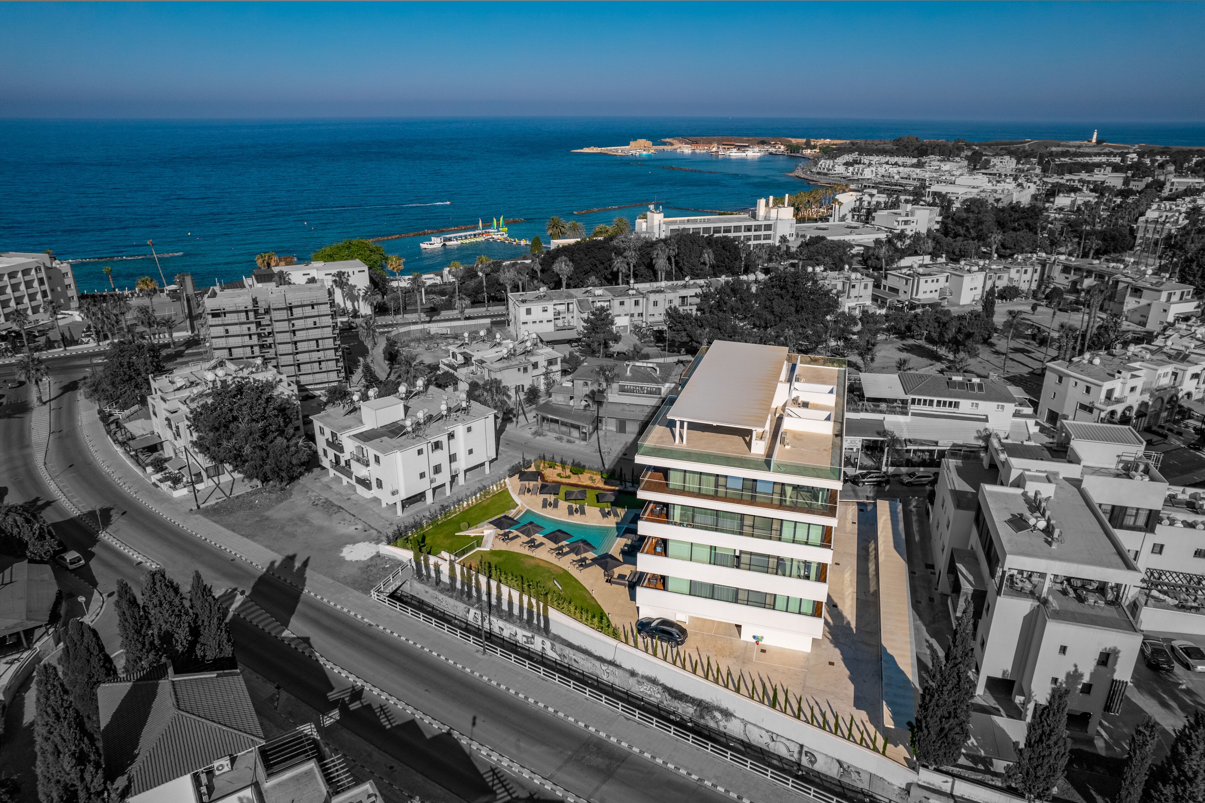 An aerial view of a coastal city with a modern hotel featuring a rooftop pool and a view of the sea.