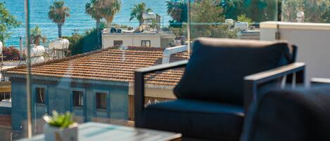 A balcony with a view of the sea, a chair, and a small table with a plant.