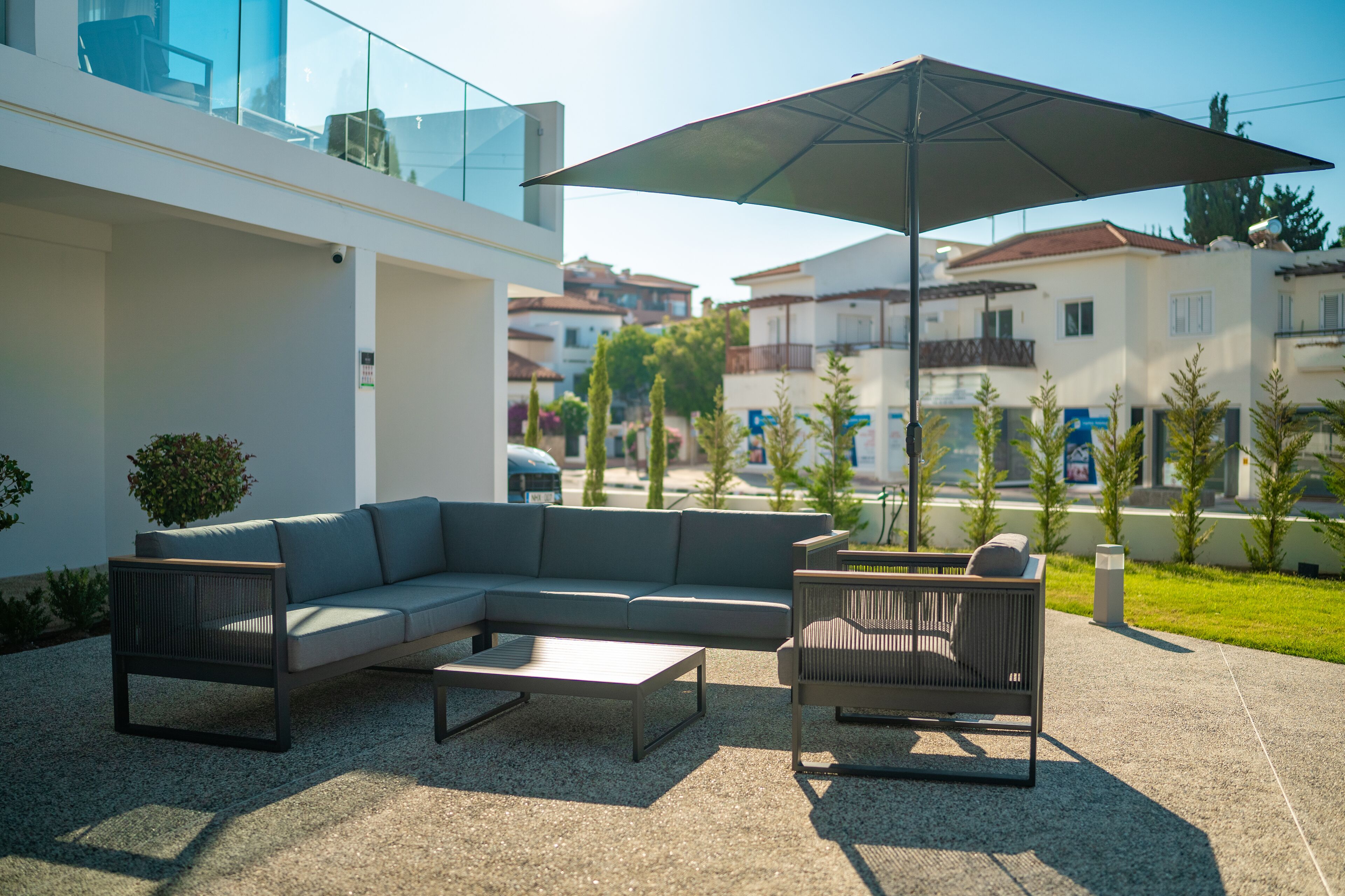 Un espacio al aire libre con un sofá seccional, una mesa de centro y una silla bajo un paraguas grande.