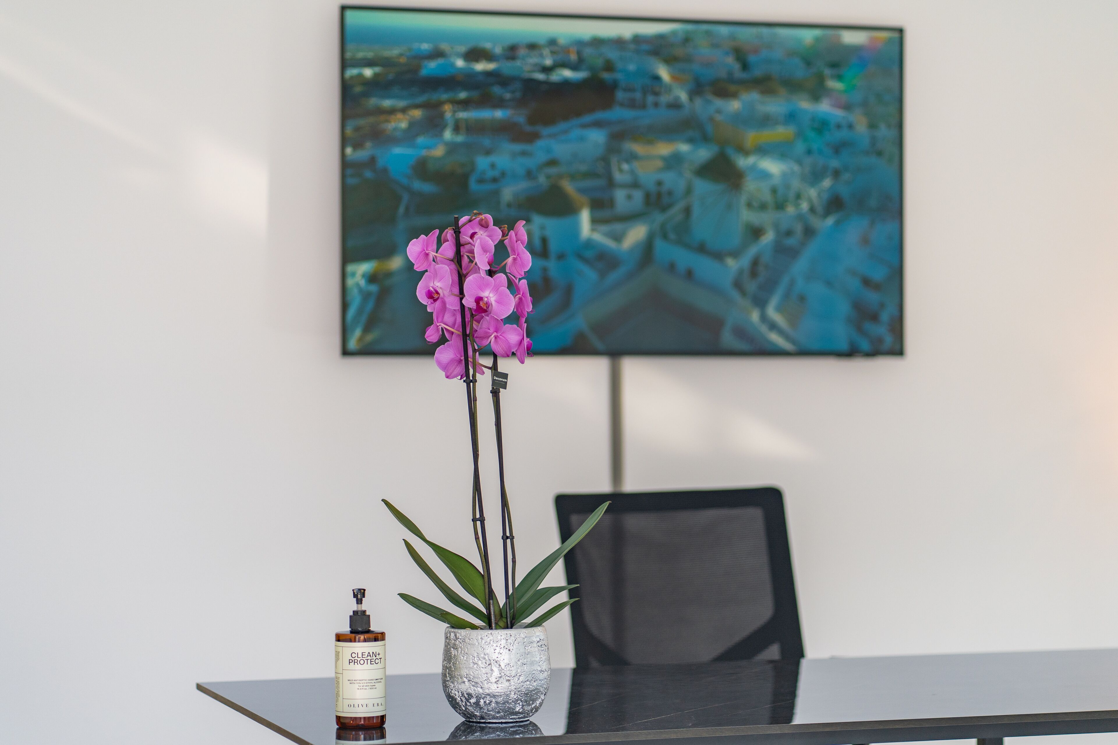 A table with a potted orchid, a bottle of olive oil, and a framed cityscape painting.