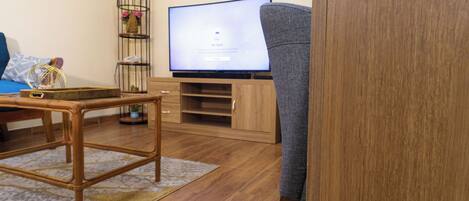 A living room with a wooden floor, a television on a stand, a grey sofa, and a small table with a basket.