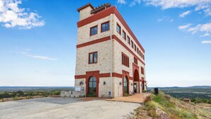 Ein mehrstöckiges Gebäude mit einer Stein-Fassade und roten Akzenten, gelegen auf einem Hügel mit freiem Blick auf die umliegende Landschaft.