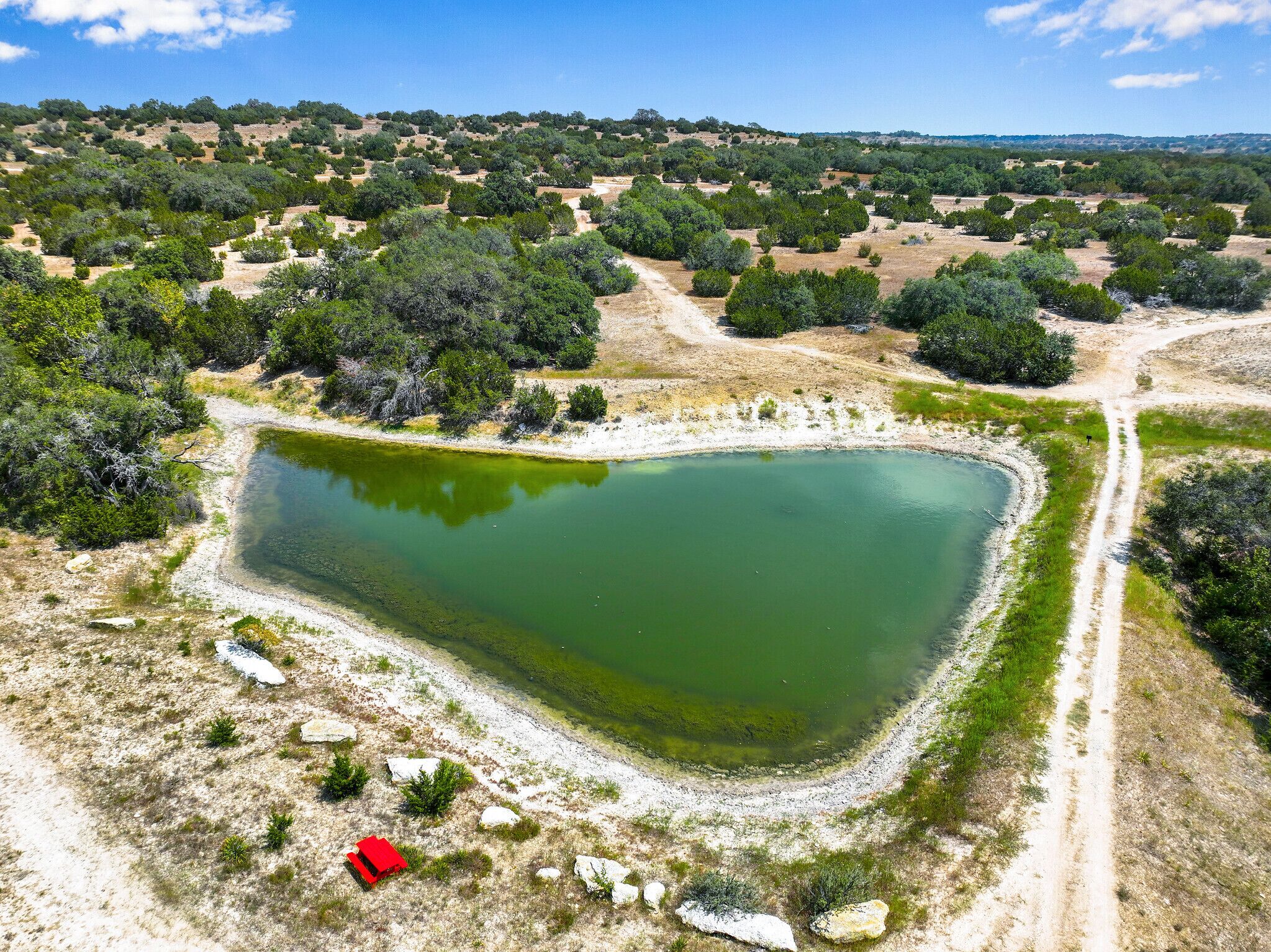 An aerial view of a large, irregularly shaped pond surrounded by sparse vegetation and a dirt path.