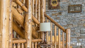 A rustic wooden staircase with a lamp and a wall sign indicating the Beehive Basin. - Luxury 4BR Beehive Basin Home | Hot Tub, Mountain Views & Sleeps 13 (Big Sky)
