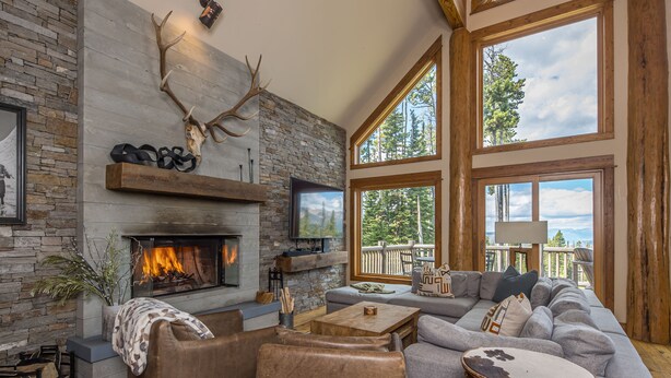 A cozy living room with a stone fireplace, a large window, and a comfortable seating area. - Luxury 4BR Beehive Basin Home | Hot Tub, Mountain Views & Sleeps 13 (Big Sky)