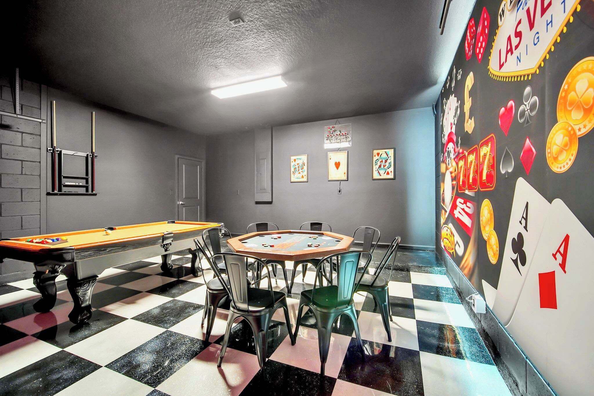 A pool table with chairs, a checkered floor, and a wall with playing card designs.