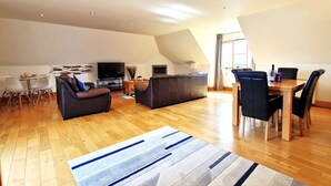 A spacious living area with a TV, sofa, and dining table. - Carnethic House Penthouse Apartment (Fowey)