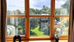 A window with a view of a garden, a pair of binoculars, and a potted orchid. - Carnethic House Penthouse Apartment (Fowey)