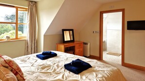 A bedroom with a large bed, a dresser, a mirror, and a television on the wall. - Carnethic House Penthouse Apartment (Fowey)