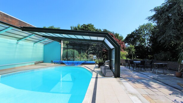A swimming pool with a glass enclosure, outdoor seating, and a clear blue sky. - Carnethic House Penthouse Apartment (Fowey)