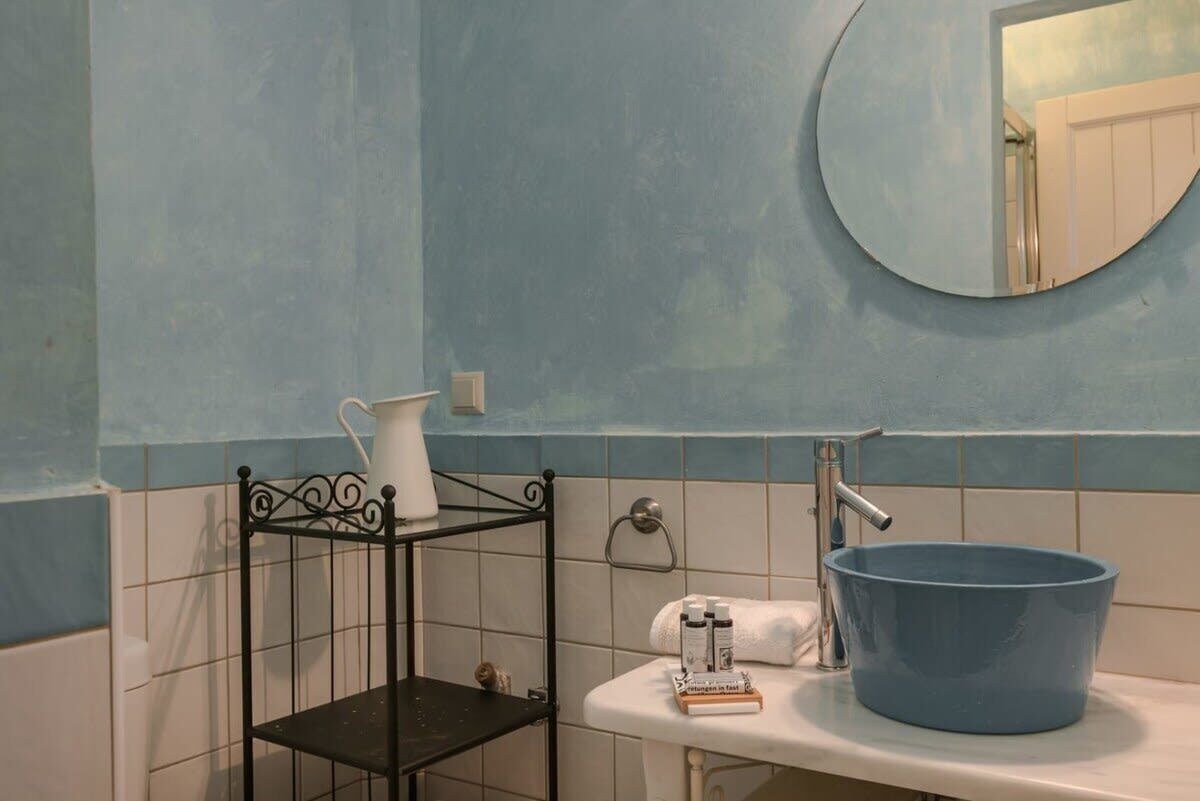 Um banheiro com uma pia azul, um jarro branco e uma prateleira preta.