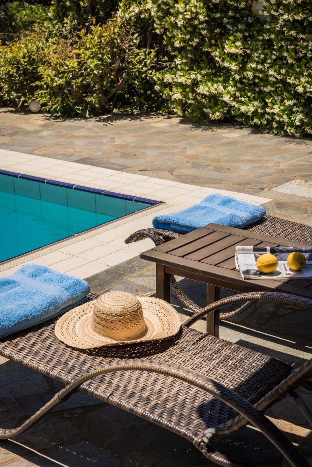 Un espace aménagé au bord de la piscine, avec un fauteuil de relaxation, une table sur laquelle sont posés des citrons et un journal, et un chapeau de paille sur le fauteuil.