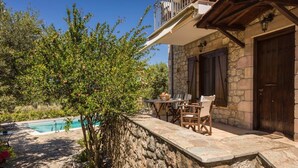 A stone-walled outdoor area with a pool, a table with chairs, and a stone building with a balcony. - Eleonas Houses - Kardamili's  Bianca Poolside Gem (Kardamyli)