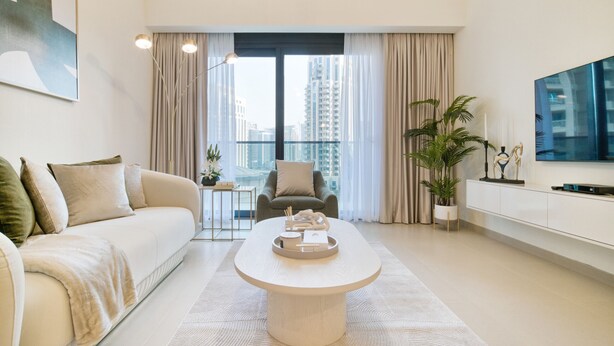 Una sala de estar moderna con sofá, mesa de centro, televisor y balcón con cortinas.