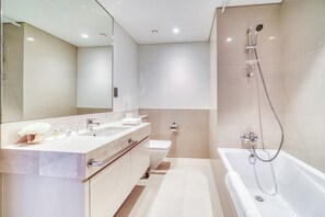 A modern bathroom with a large mirror, two sinks, a toilet, and a bathtub with a showerhead.