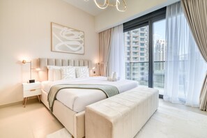 A modern bedroom with a large bed, bedside tables, a bench, and a city view through large windows.
