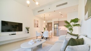 Una sala de estar moderna con un televisor de pantalla plana, un comedor con mesa y sillas, y una cocina con refrigerador.