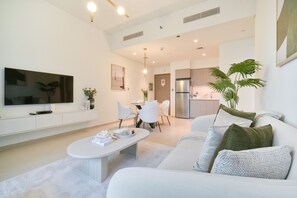 Ein modernes Wohnzimmer mit Flachbildfernseher, eine Essecke mit Tisch und Stühlen sowie eine Küche mit Kühlschrank.