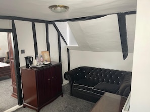 A room with a dark wooden dresser, a black tufted sofa, and a white ceiling with a light fixture. - The French Partridge (Northampton)