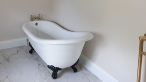 Een witte pootbad met zwarte poten, een gouden kraan en een lijst met een foto aan de muur.