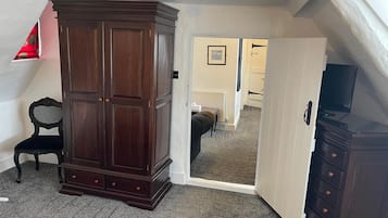 Una habitación con un armario grande de madera oscura, una pequeña silla negra y un televisor sobre un mueble.