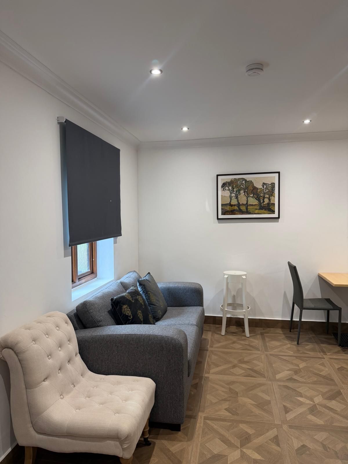 Una sala de estar con un sofá gris, un sillón blanco, una mesita y un cuadro en la pared.