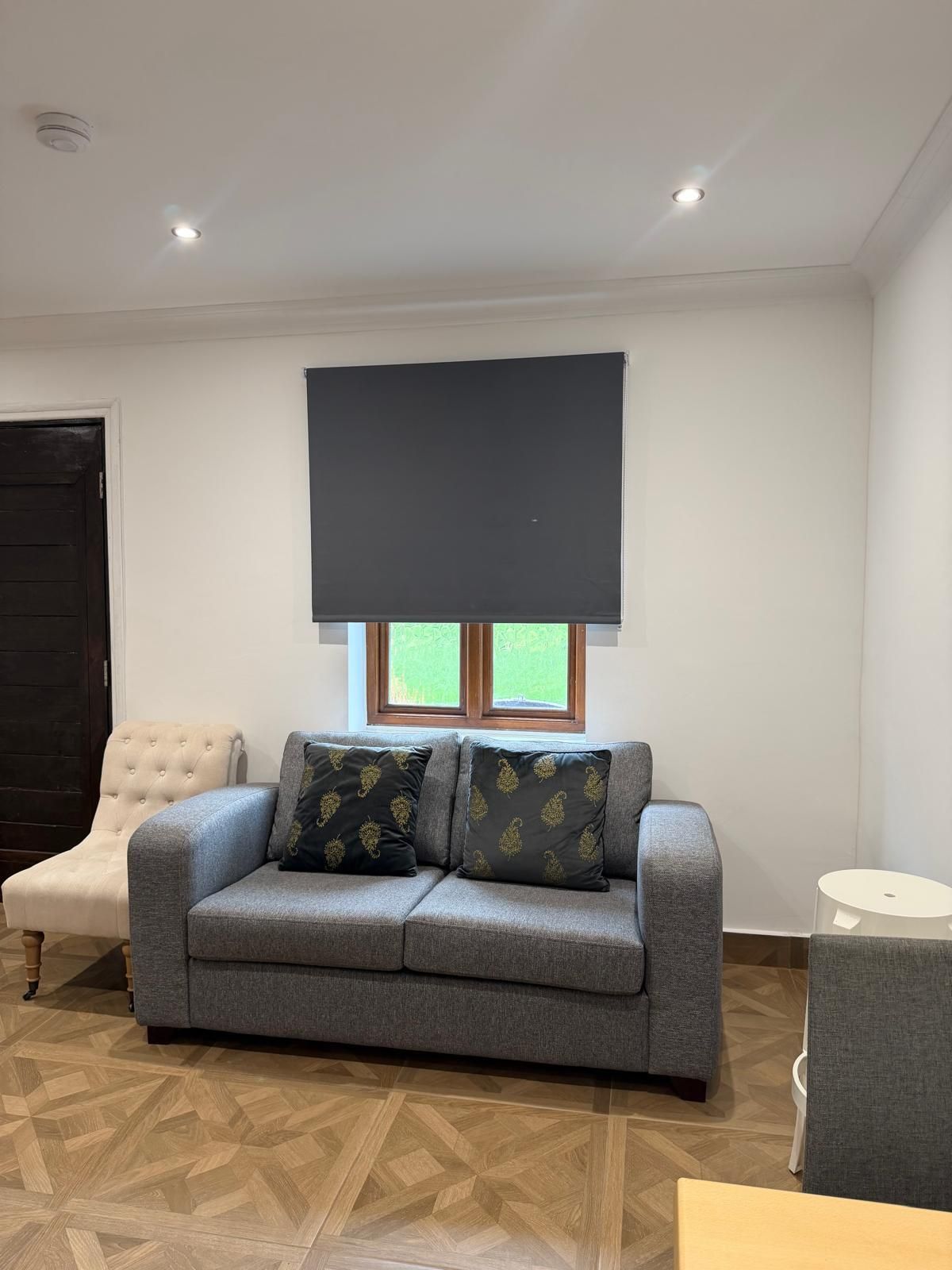 A living room with a grey sofa, two patterned cushions, a black screen, and a wooden floor.