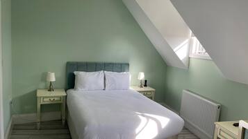 A bedroom with a sloped ceiling, a bed with white bedding, two bedside tables with lamps, and a radiator.