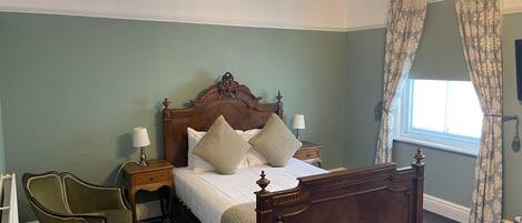 A bedroom with a four-poster bed, two bedside tables, a chair, and a window with curtains.