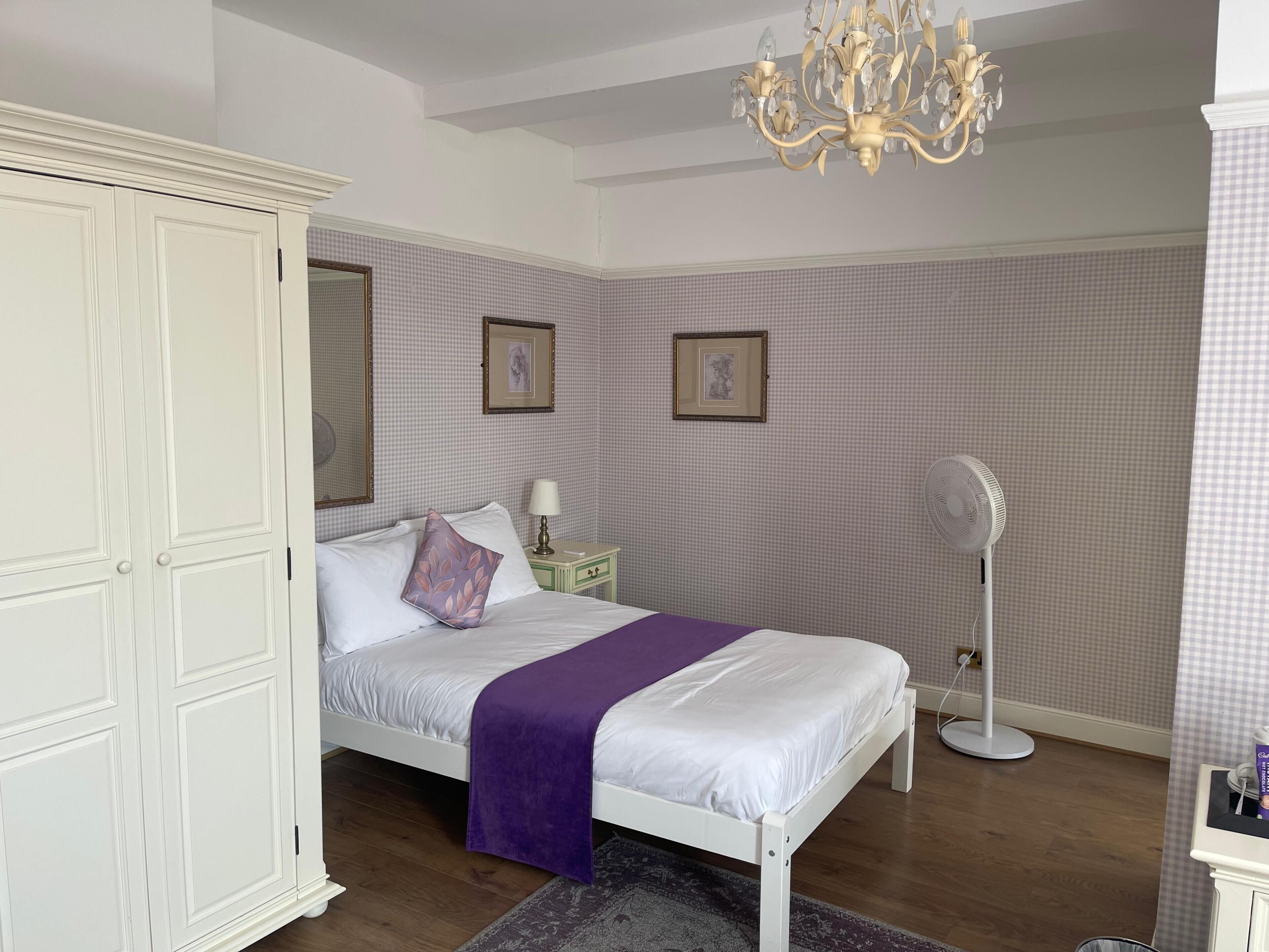 A bedroom with a bed, a wardrobe, a bedside table with a lamp, a fan, and a chandelier.