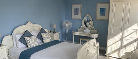 A bedroom with a white bed, a nightstand, a dresser, a mirror, and a fan.