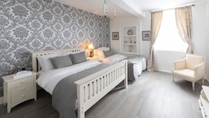 Een slaapkamer met twee bedden, een nachtkastje, een lamp, een stoel en een raam met gordijnen.