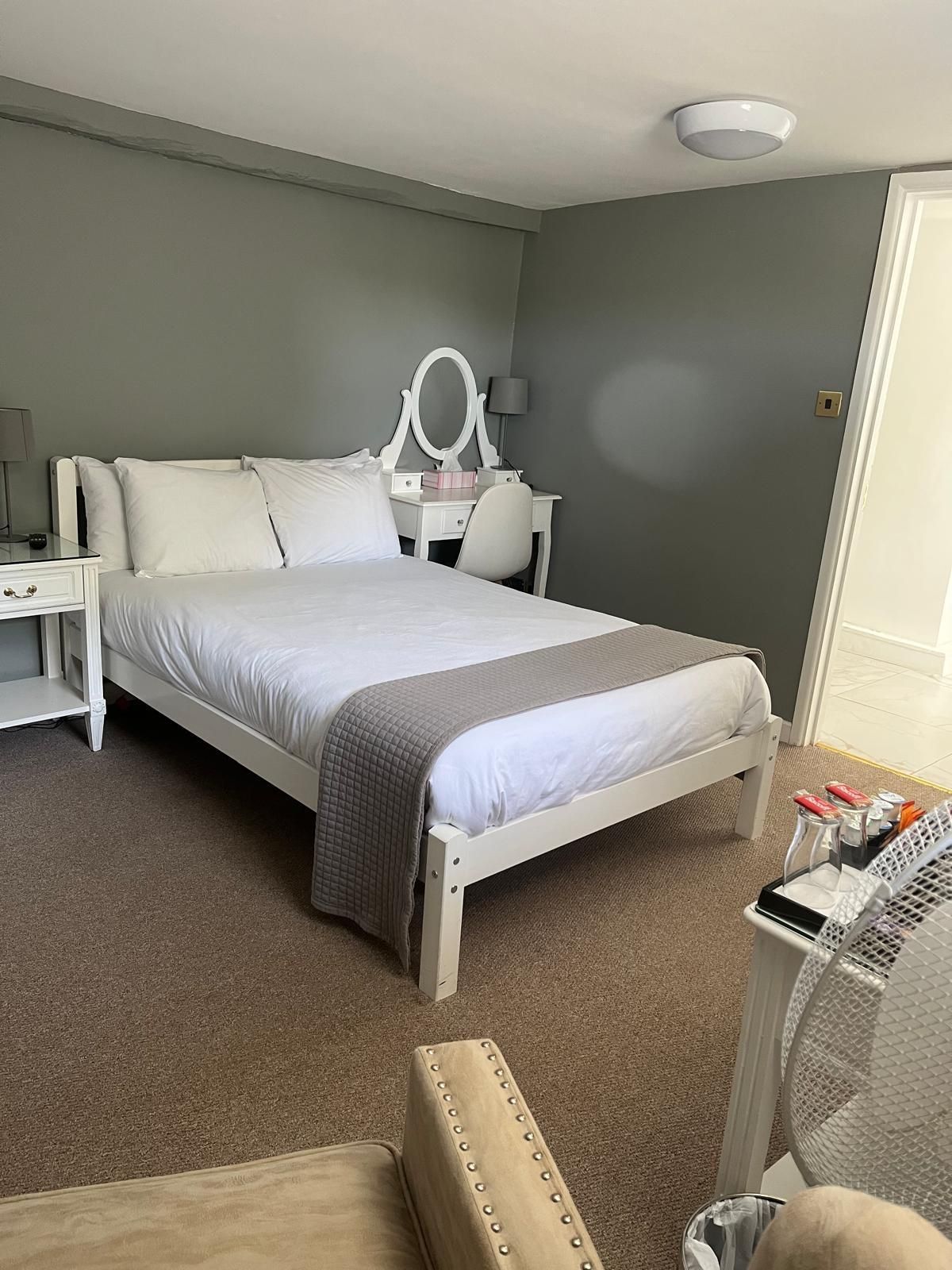 Una habitación de hotel ordenada con cama, mesita de noche, lámpara y espejo.