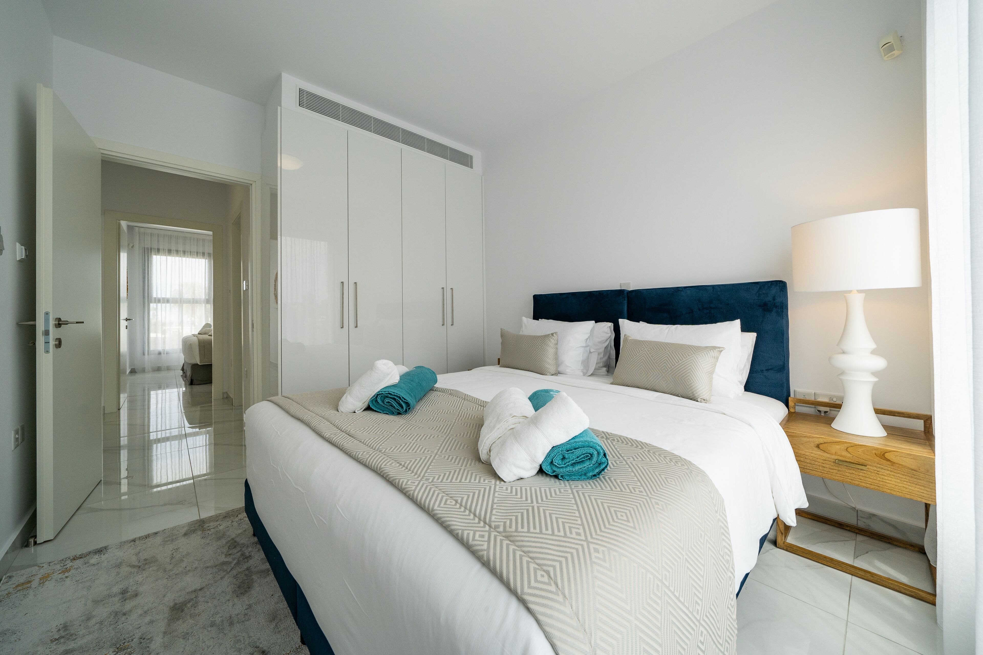 Quarto de hotel com cama, mesa de cabeceira, luminária e guarda-roupa.