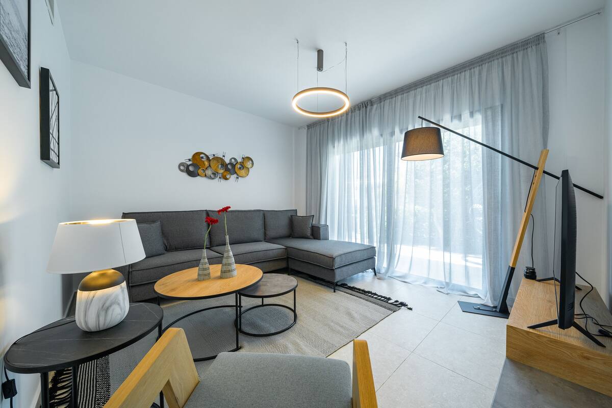 Un salon moderne avec un canapé d’angle gris, une table basse ronde, un lampadaire et une œuvre d’art murale.