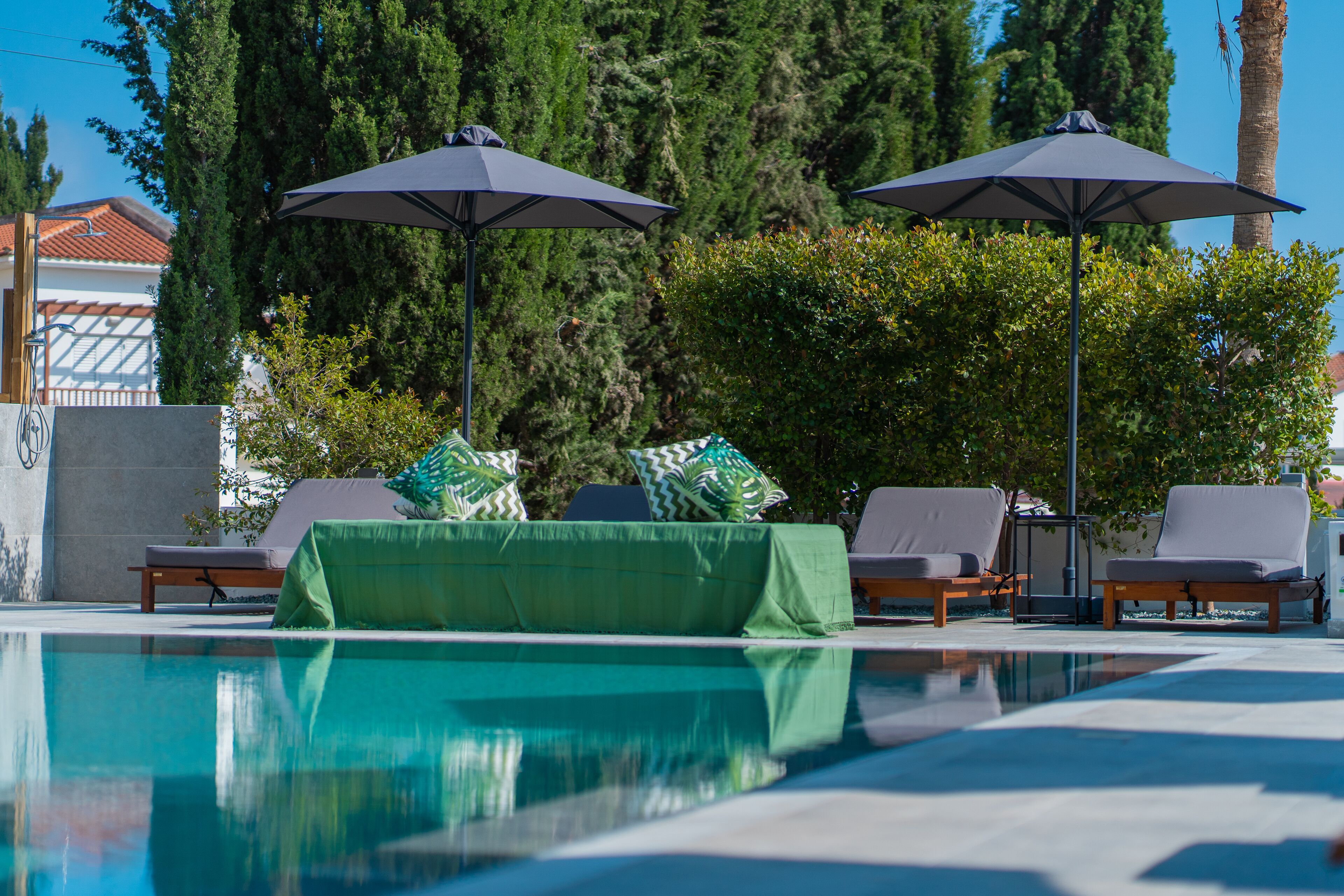 Une piscine entourée de verdure, avec des chaises longues et des parasols, sous un ciel dégagé.