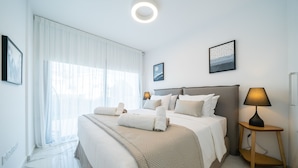 A hotel room with a large bed, two bedside tables, a nightstand, and a window with sheer curtains. - Silver Park by Deserve (Paphos)