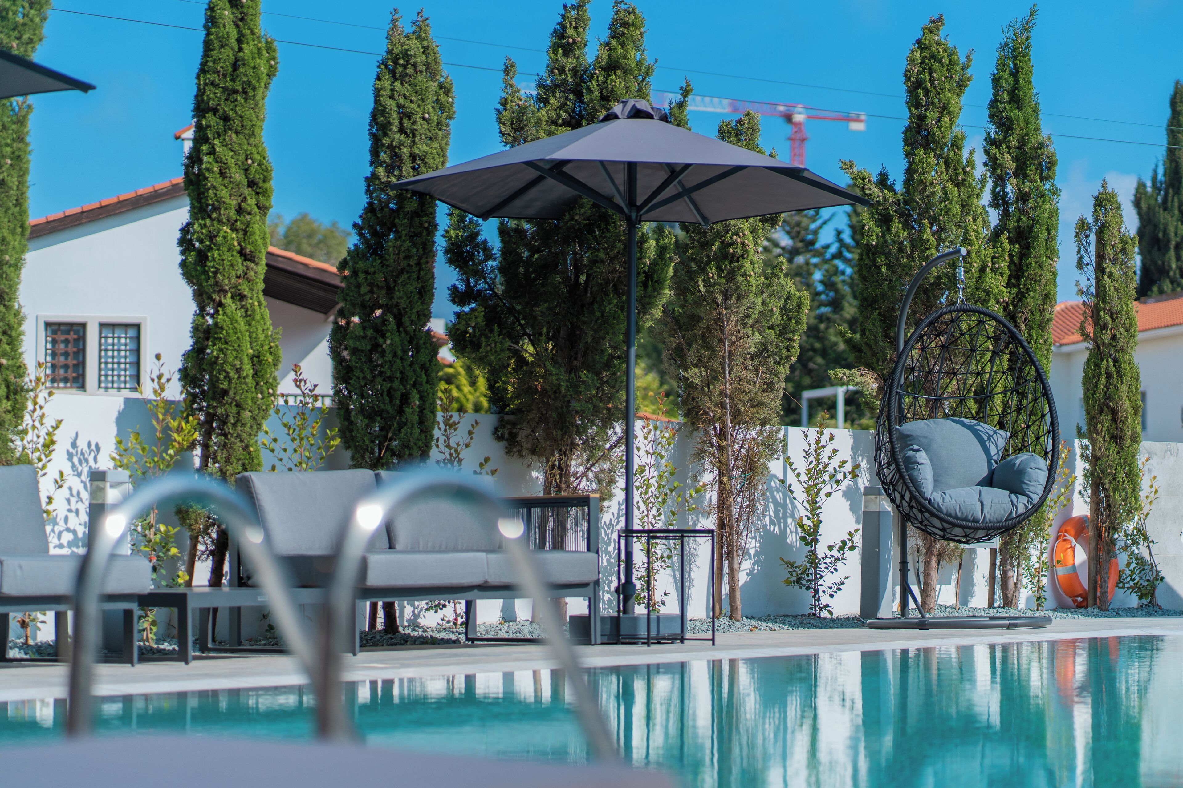 A pool area with lounge chairs, a hanging chair, and an umbrella.