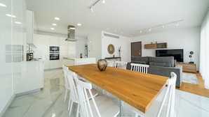 A modern kitchen with white cabinets, a wooden dining table, and white chairs. - Silver Park by Deserve (Paphos)