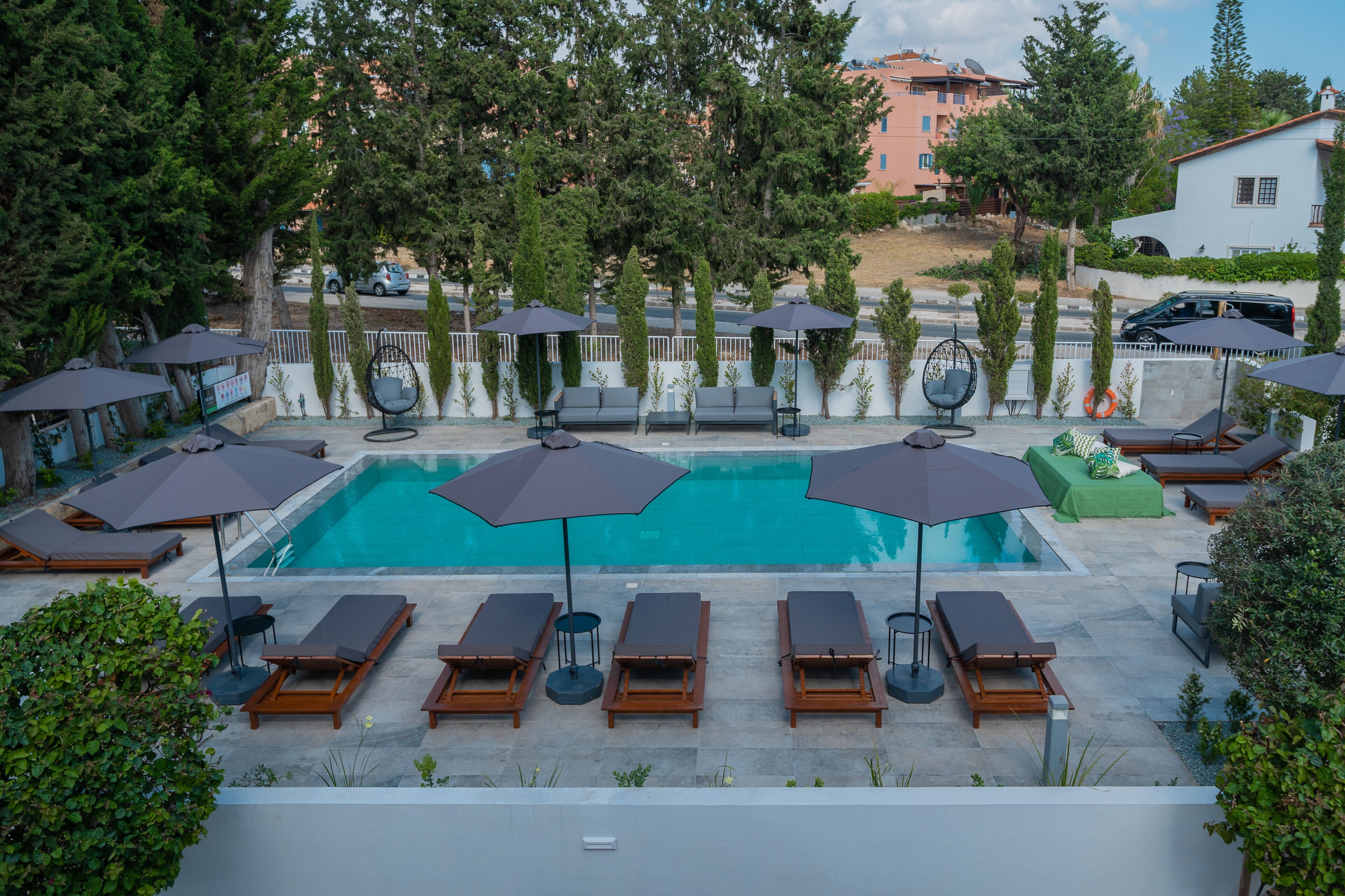 A rooftop pool area with sun loungers and umbrellas, surrounded by trees and buildings.