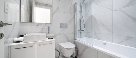 Un baño moderno con un lavabo blanco, inodoro y bañera, todo sobre baldosas de mármol.